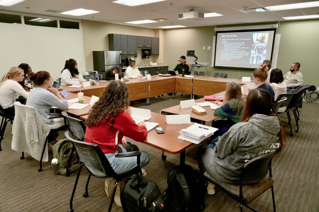 Wide shot of classroom with students gathered around rectangle of tables