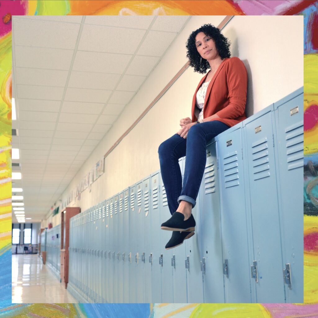 Anna Haskins sitting on blue lockers in an empty school hallway