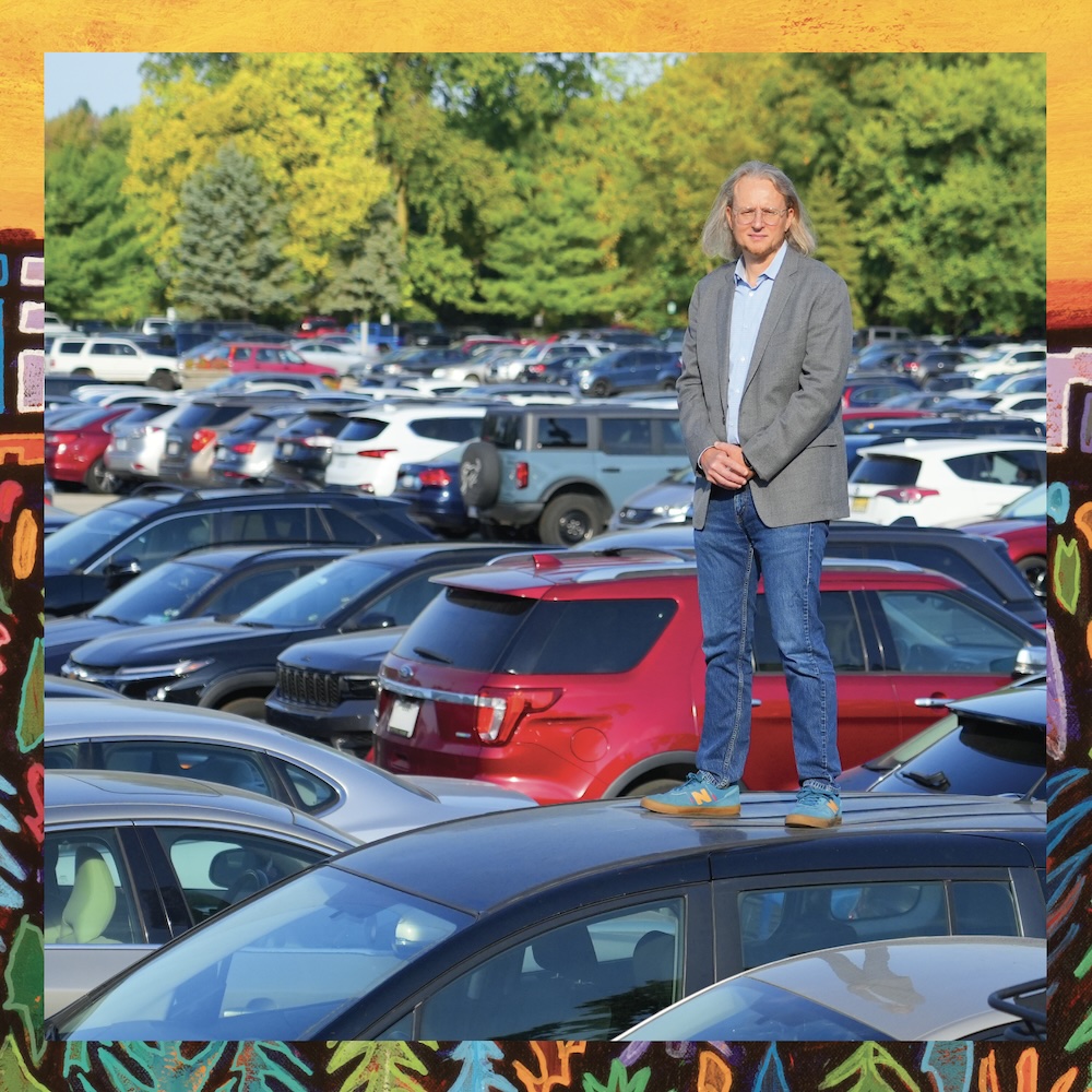 Roy Scranton standing on a car in a parking lot