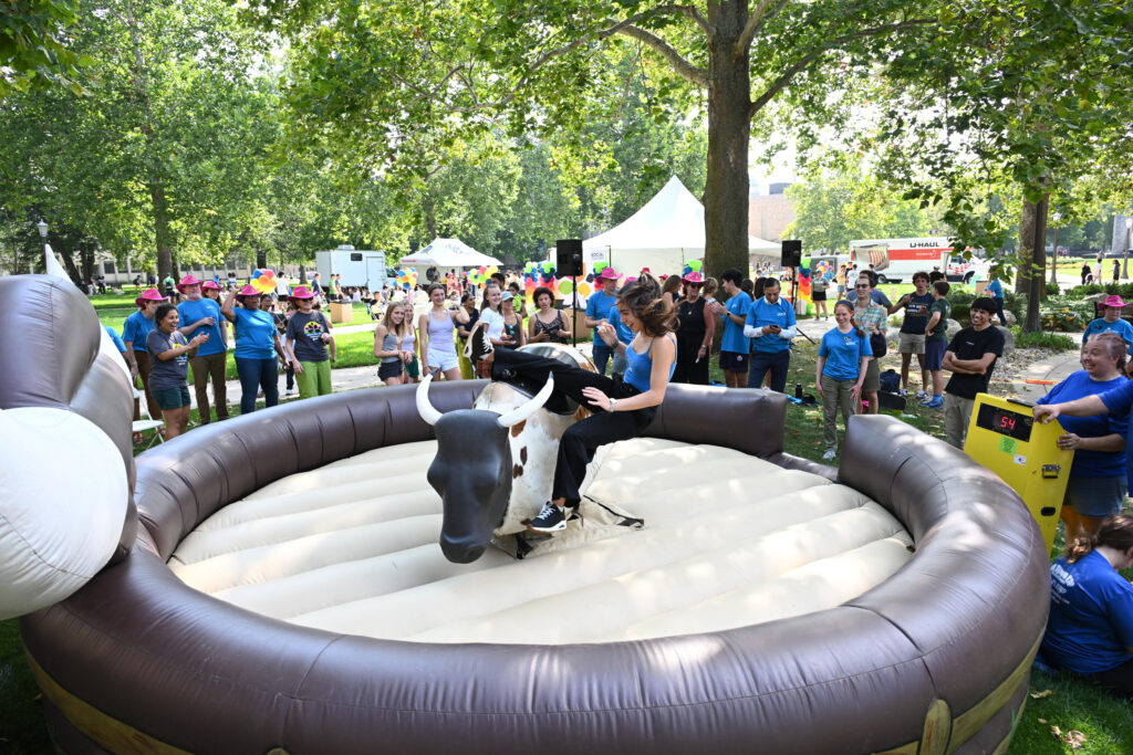 A woman rides a mechanical bull outside of Geddes Hall