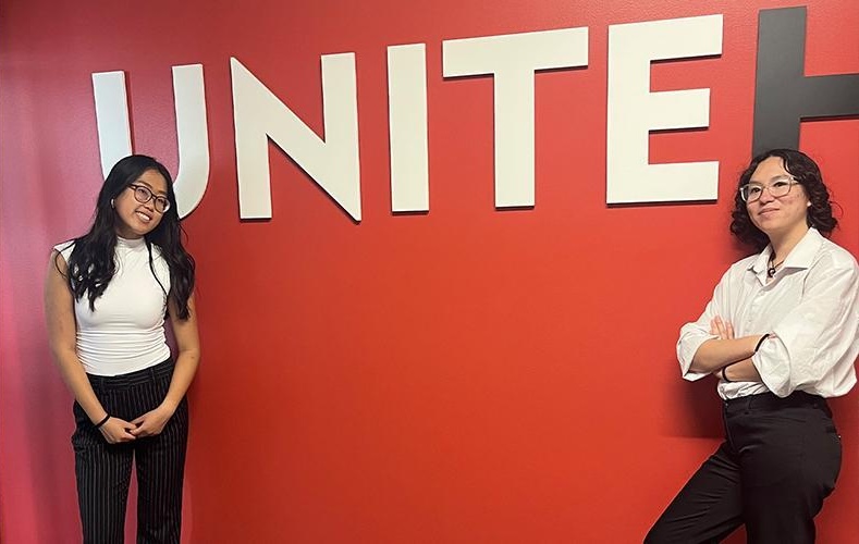 Two students stand in front of Unite sign on red wall